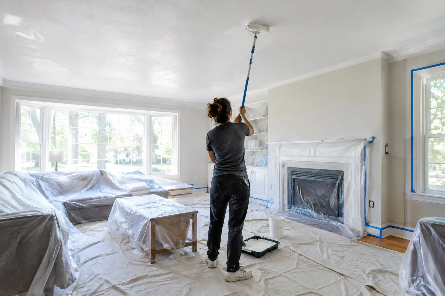 Un plafond est peint au rouleau sur une perche dans une pièce protégée.