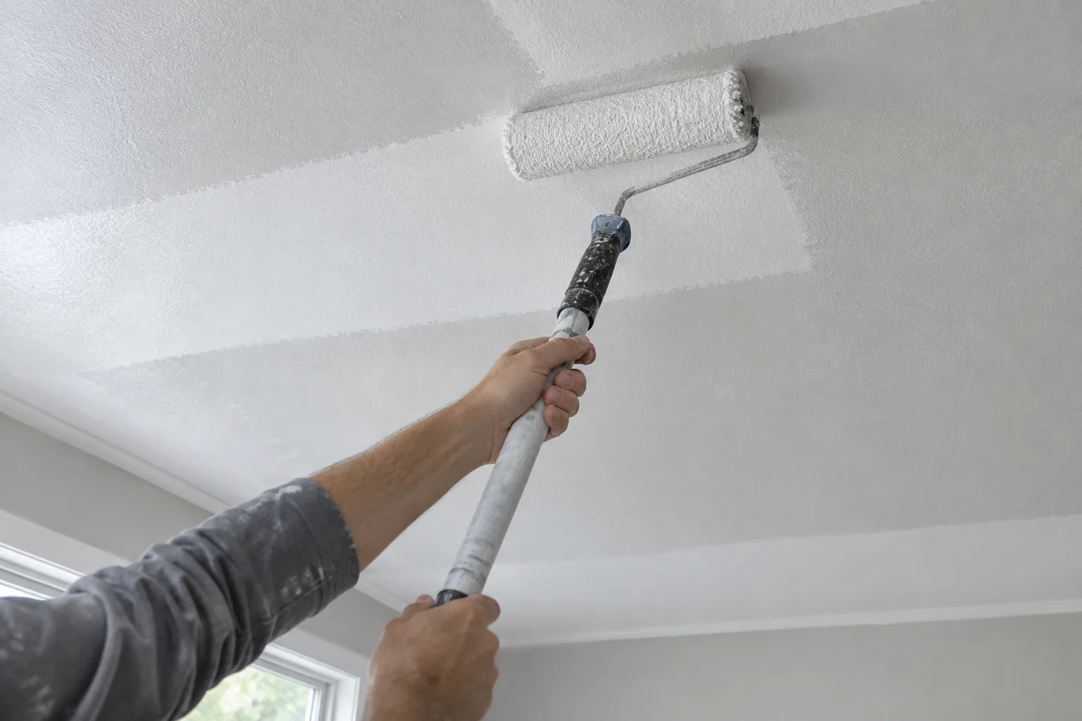 Un rouleau dépose la peinture en bandes régulières sur un plafond.