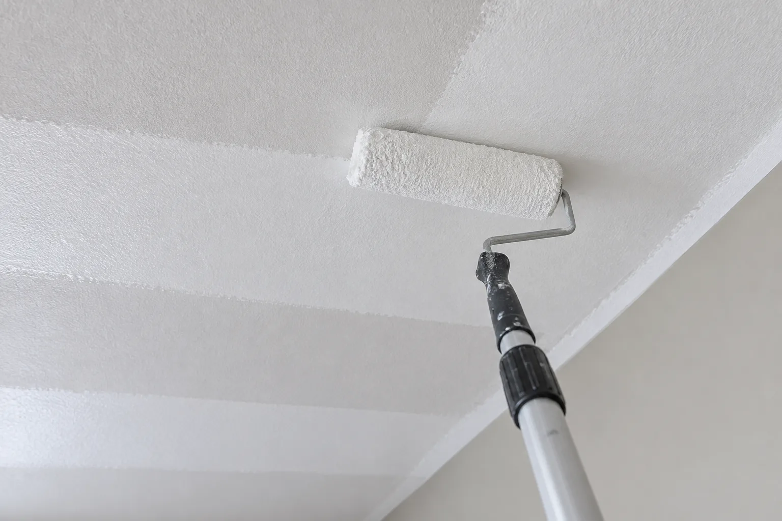 Un rouleau sur perche applique la peinture au plafond par bandes régulières.