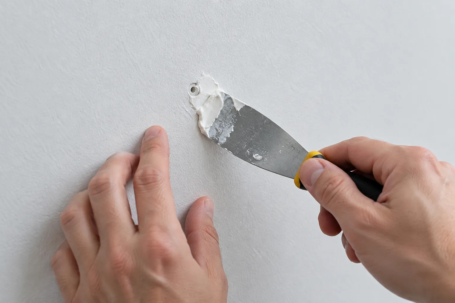 Un couteau à enduire presse de l’enduit de rebouchage dans un petit trou du mur.